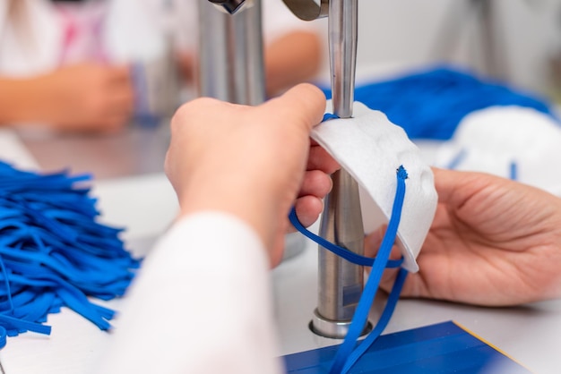 Una mujer trabaja en una fábrica para la fabricación de máscaras médicas con nanofibras y bucles de soldadura con ultrasonido en una máquina Coronavirus y Covid19 Protección Closeup