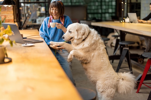 Una mujer trabaja en una laptop mientras se sienta con su perro en una cafetería moderna