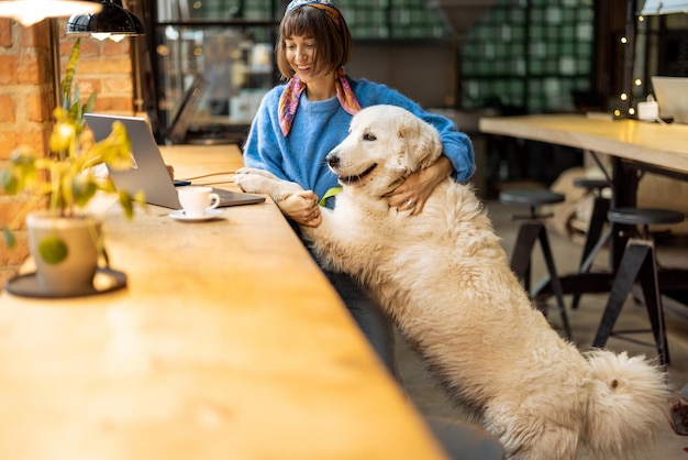 Una mujer trabaja en una laptop mientras se sienta con su perro en una cafetería moderna