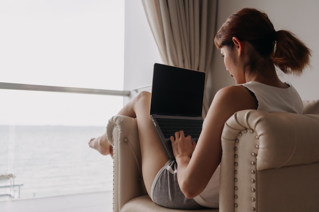 La mujer trabaja y se relaja con la computadora portátil en el sofá concepto de trabajo del hotel