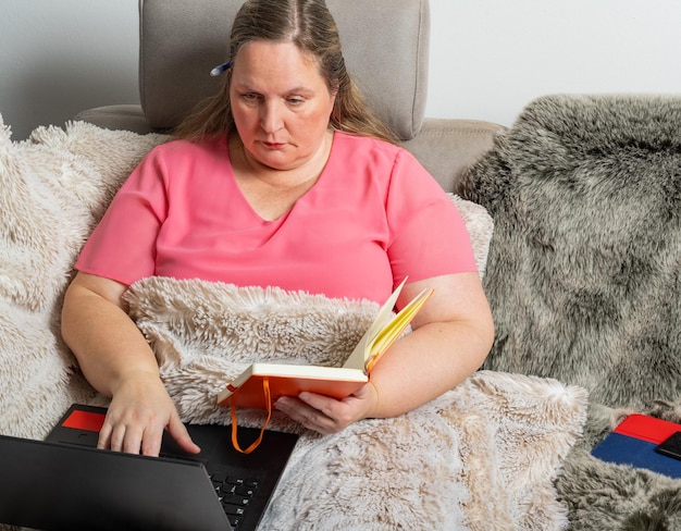 La mujer trabaja en un sofá con una computadora portátil, una tableta y un teléfono móvil en la oficina del hogar