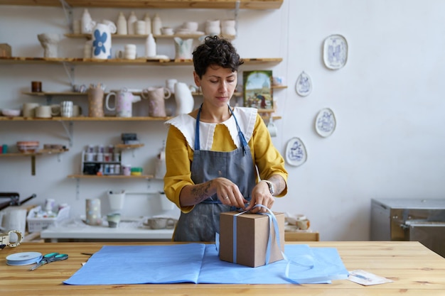 Mujer trabaja en una tienda de cerámica artesanal o en un estudio empacando cerámica en una caja de regalo para entregarla al consumidor