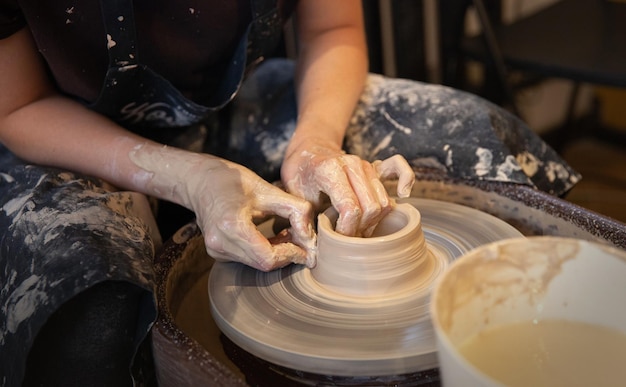 Una mujer trabaja en un torno de alfarero Las manos forman una taza de arcilla húmeda en un torno de alfarero Concepto artístico