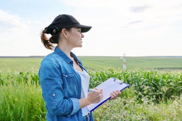 Mujer trabajadora agrícola con carpeta de trabajo en campo de maíz verde, mujer trabajando en la granja, analiza la cosecha, copia espacio