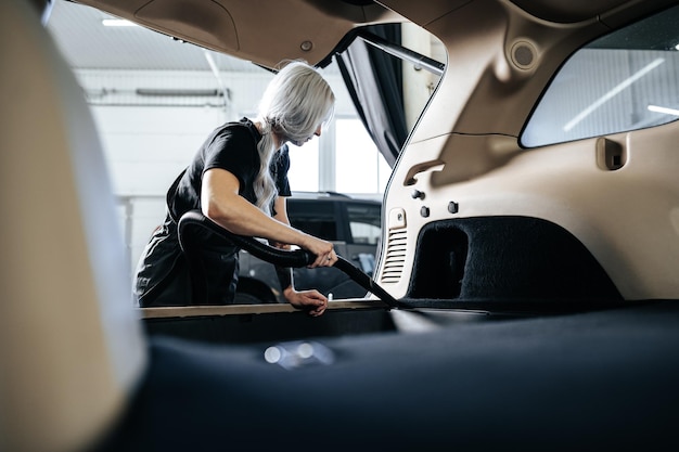 Mujer trabajadora aspiradora limpiando el interior del polvo dentro del auto en lavado de autos