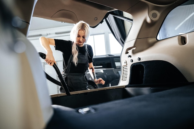 Mujer trabajadora aspiradora limpiando el interior del polvo dentro del auto en lavado de autos