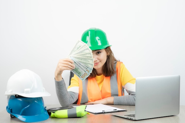 Mujer trabajadora con chaleco naranja y casco verde sentada en el escritorio. foto de alta calidad