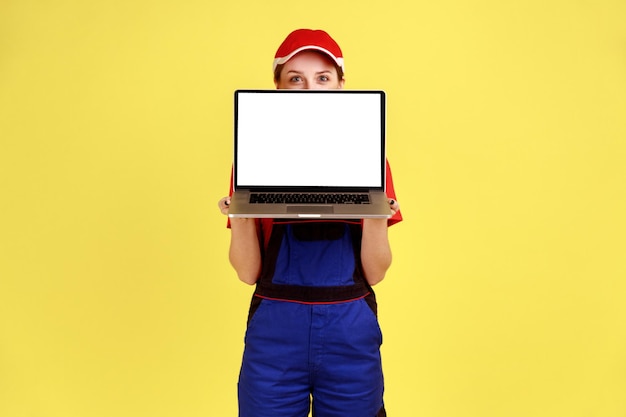 Mujer trabajadora desconocida de pie cubriendo la cara con una computadora portátil con pantalla en blanco para la promoción