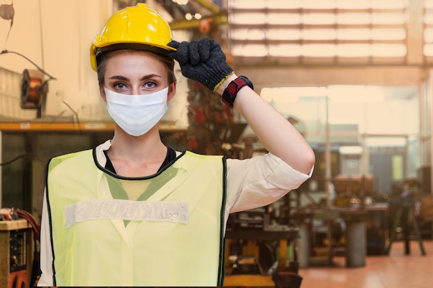 Mujer trabajadora de fabricación de enfermedades con cara de cubierta de máscara se encuentra con el fondo de la fábrica interior