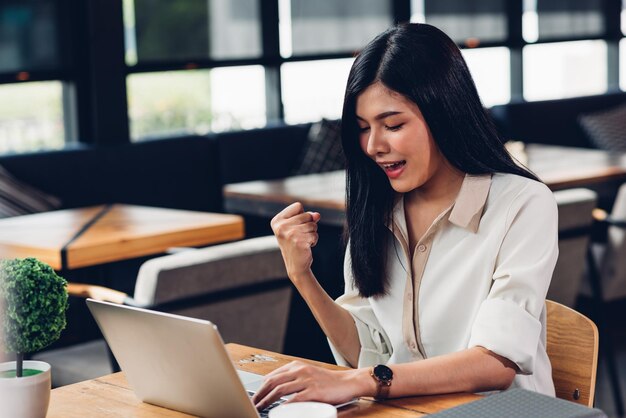 Mujer trabajadora independiente con computadora portátil, con gusto obtiene los resultados en la cafetería