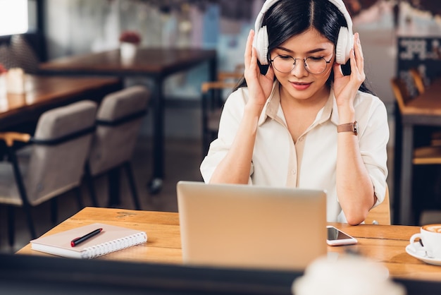 Mujer trabajadora independiente de estilo de vida y computadora portátil que escucha radio musical en una cafetería
