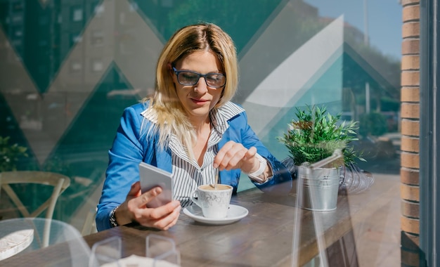 Mujer trabajadora joven que mira el teléfono celular en un café