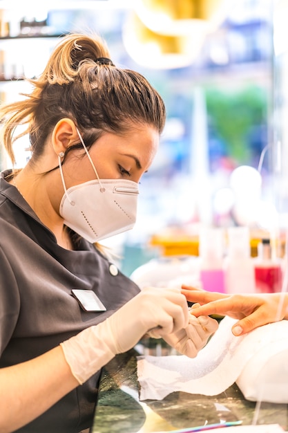 Mujer trabajadora con máscara en tratamiento de uñas. Reapertura después de la pandemia corod-19. Salón de manicura y pedicura. Coronavirus