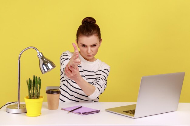 Mujer trabajadora de oficina sentada en el lugar de trabajo con una computadora portátil amenazando y apuntando con el dedo a la cámara