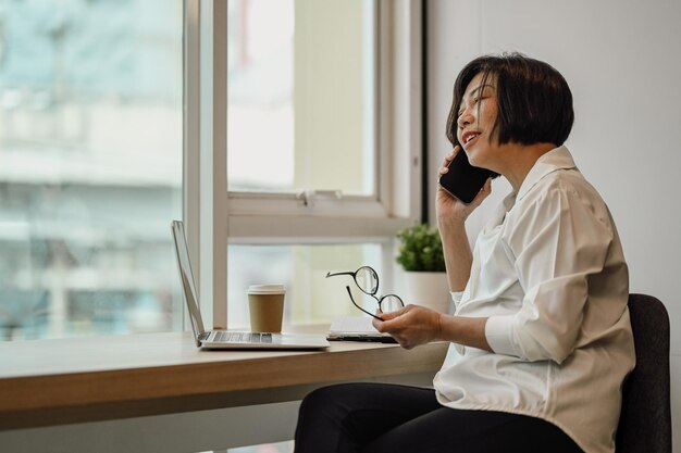 Mujer trabajadora de primer plano con la mano sosteniendo una taza de papel de café caliente y usando el teléfono móvil