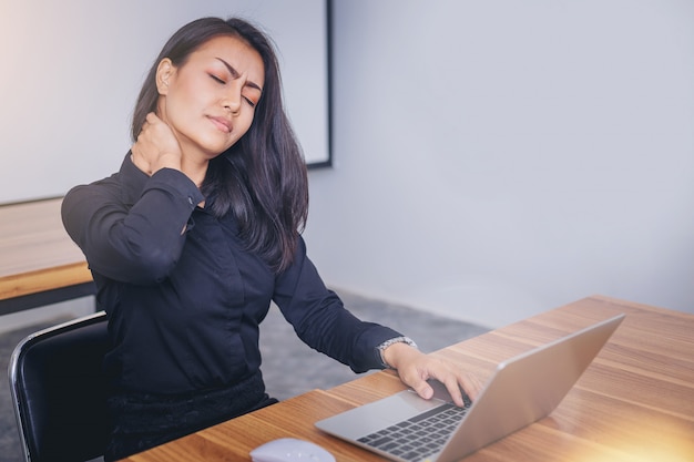 Mujer trabajadora que sufre por dolor de cuello al trabajar con una computadora portátil