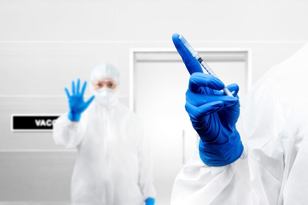Mujer trabajadora de salud con traje protector y guantes sosteniendo vacunas covid 19 en el hospital