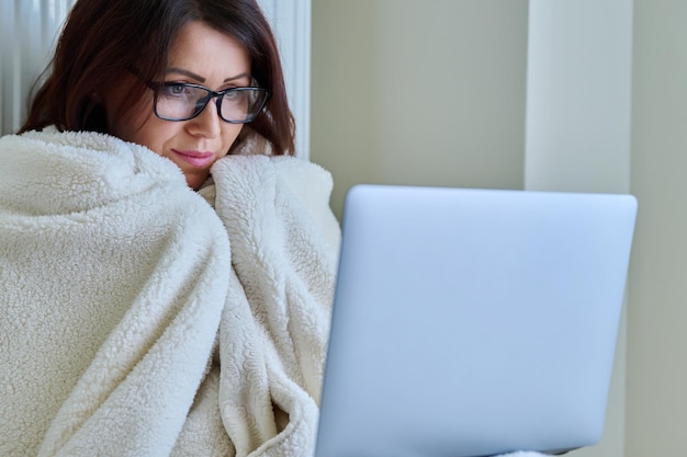 Mujer trabajando en casa con portátil calentándose con manta y radiador de calefacción