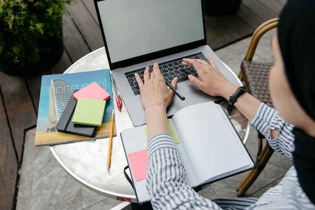 Mujer trabajando en una computadora portátil al aire libre con un cuaderno y notas adhesivas