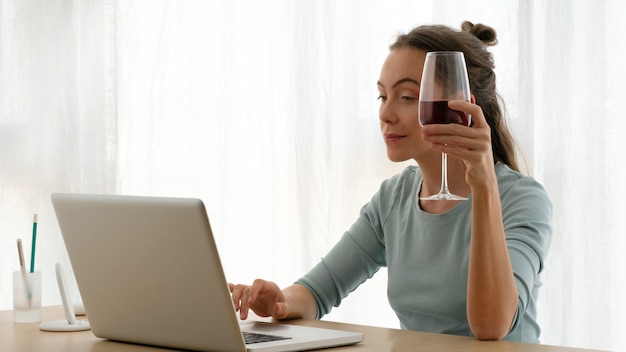 Mujer trabajando en una computadora portátil con una copa de vino