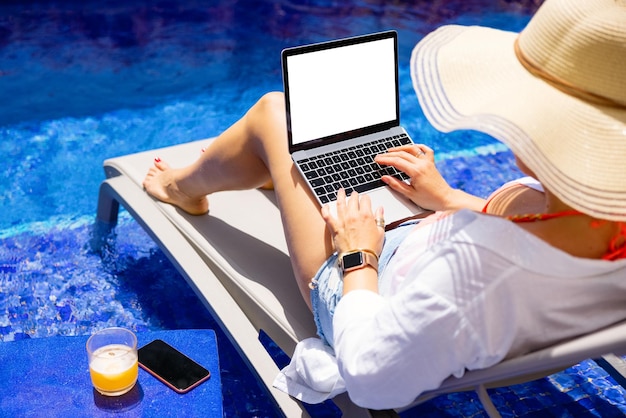 Mujer trabajando en una computadora portátil junto a la piscina