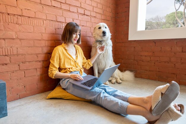 Mujer trabajando en una computadora portátil mientras está sentada con su perro en casa