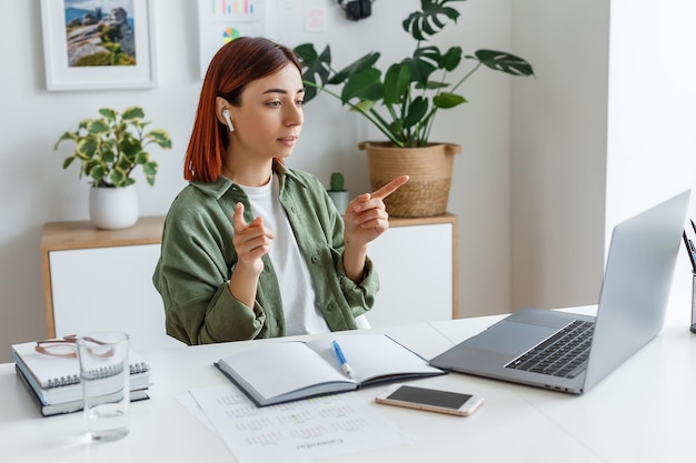 Mujer trabajando de forma remota en casa con ordenador portátil Joven empresaria hablando a través de auriculares inalámbricos