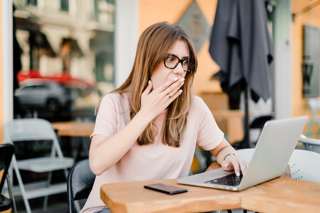 Mujer trabajando remotamente con laptop y teléfono en cafe