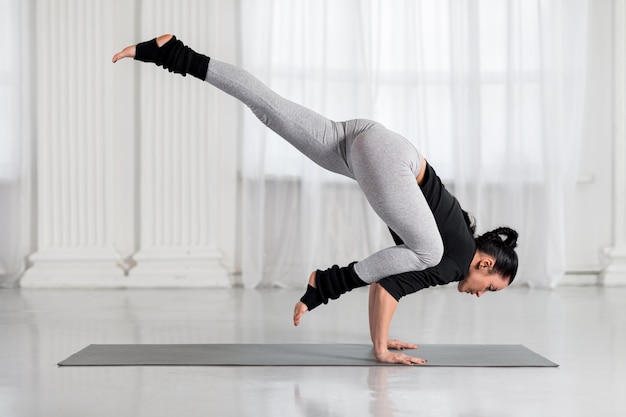 Mujer trabajando en el salón blanco, haciendo yoga de equilibrio del brazo parada de manos