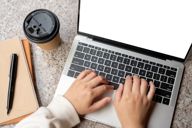Una mujer trabajando en su computadora portátil en una mesa escribiendo en el teclado Una maqueta de computadora portátil con pantalla blanca