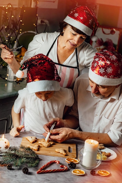 Mujer de tradición familiar de Navidad viendo a su nieto con el abuelo preparar pan de jengibre en la cocina