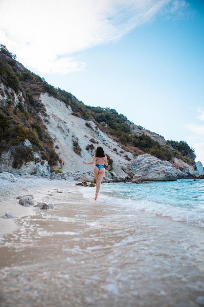 Mujer en traje de baño azul corriendo por la playa del mar