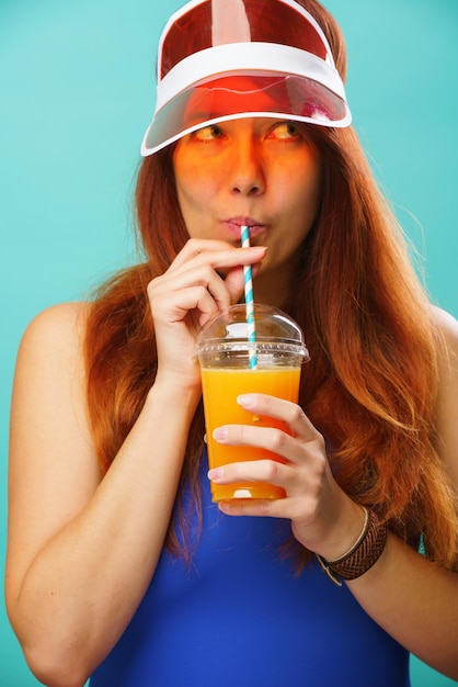 Mujer con traje de baño azul y sombrero bebe jugo de fruta de una taza