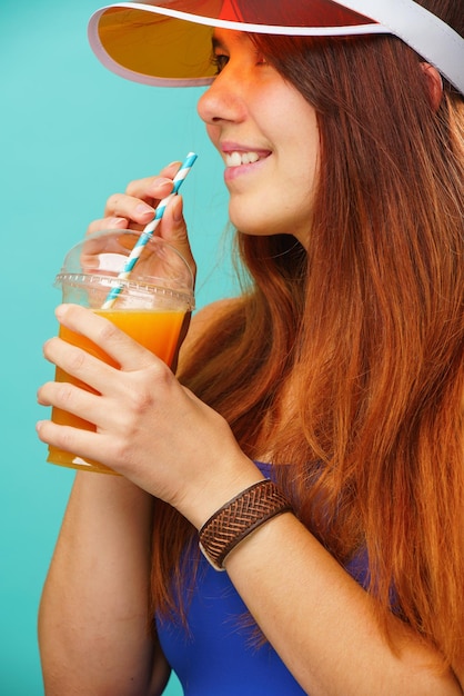 Mujer con traje de baño azul y sombrero bebe jugo de fruta de una taza