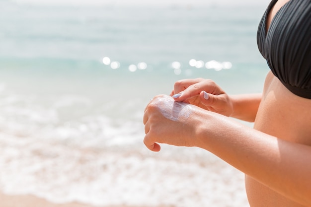 Mujer en traje de baño está aplicando crema solar en su mano con su dedo en el fondo del mar.