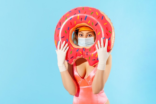 Mujer en traje de baño mirando a través del anillo de goma, usando mascarilla higiénica y guantes quirúrgicos para prevenir el coronavirus contagioso en la playa del resort, descanso y vacaciones de verano con covid-19. foto de estudio