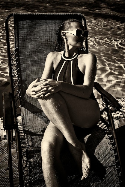 Mujer en traje de baño negro y gafas de sol blancas tomando el sol en una tumbona