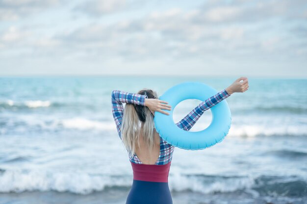 Mujer en traje de baño de una pieza con anillo inflable azul en playa tropical