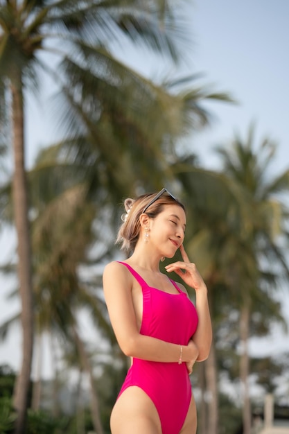 Mujer en traje de baño de una pieza rosa relajándose en el fondo del árbol de coco de la playa tropical