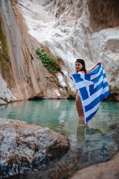 Mujer en traje de baño rojo con bandera de Grecia Dimosari cascada en la isla de Lefkada