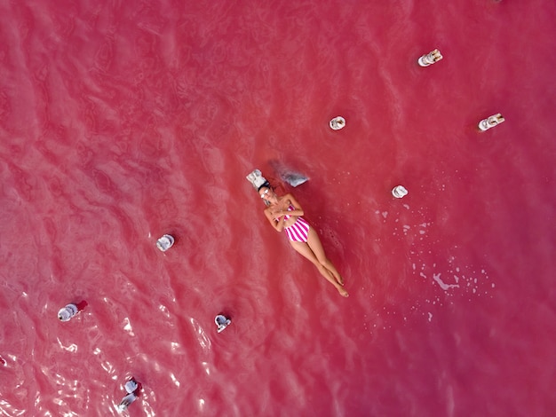 Mujer en traje de baño rosa se encuentra en un puente de madera en ruinas en medio de un lago rosa en verano