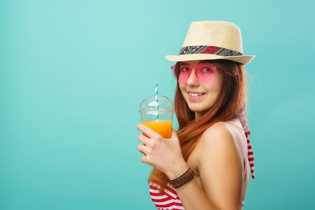 Mujer con traje de baño y sombrero bebe jugo de fruta de una taza