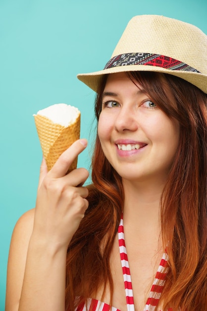 Una mujer con traje de baño y sombrero de paja come helado de una taza sobre un colorido fondo turquesa