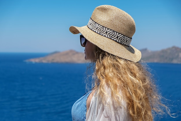 Mujer en traje de baño vestido blanco y sombrero de paja en la terraza blanca balcón Vista al mar