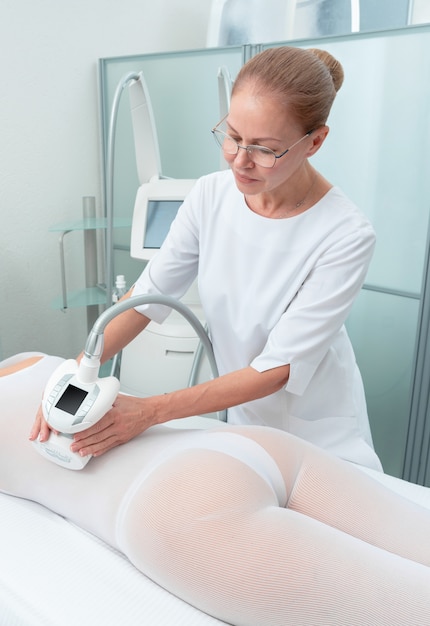 Mujer en traje blanco especial recibiendo masaje anticelulítico en un salón de spa. GLP y tratamiento de contorno corporal en clínica.