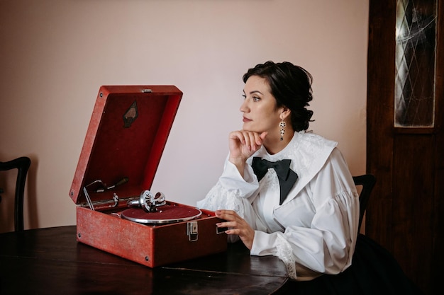 Mujer en traje de blusa vintage cerca de gramófono en viejos vestidos históricos interiores trajes vintage