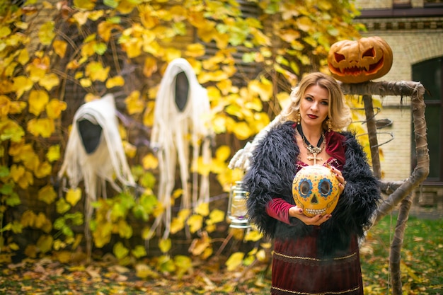 Mujer en traje de bruja está conjurando la mesa de una hechicera con calaveras y calabazas decoradas