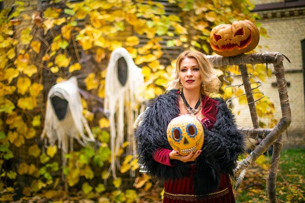 Mujer en traje de bruja está conjurando la mesa de una hechicera con calaveras y calabazas decoradas