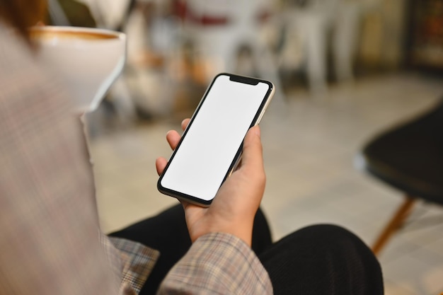 Mujer en traje elegante bebiendo café y usando teléfono móvil en una cafetería Pantalla vacía para su mensaje de texto publicitario