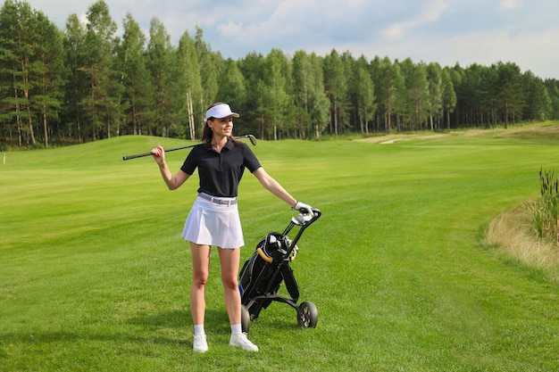 Mujer en traje de golf de verano con estilo caminando con bolsa de conductores en un hermoso campo verde para el juego de golf.